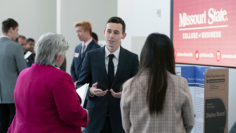 Missouri State student speaking with others at a symposium.